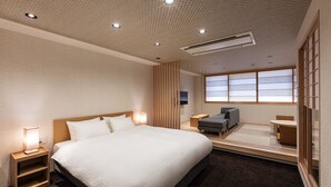 Ein modernes Hotelzimmer mit einem großen Bett, Nachttischen, einer Sitzecke mit einer Couch und einem kleinen Tisch sowie einem großen Fenster, das für natürliches Licht sorgt.