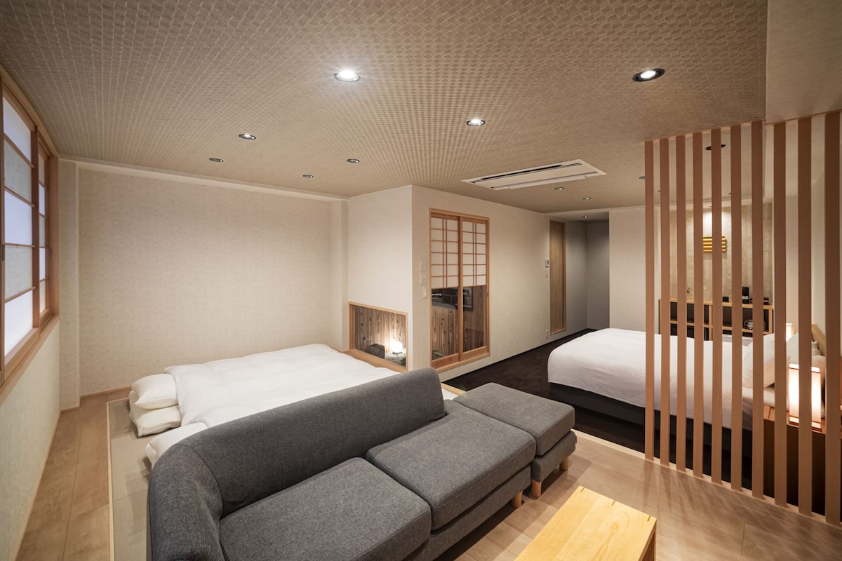 A modern hotel room with a sofa, two beds, a wooden partition, and a traditional sliding door.
