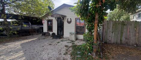 A house with a gravel driveway, a wooden fence, and a tree in the foreground.