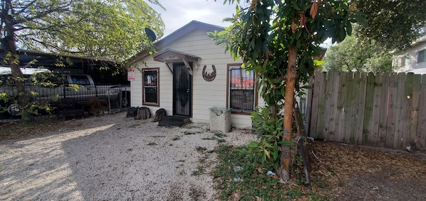 A house with a gravel driveway, a wooden fence, and a tree in the foreground.
