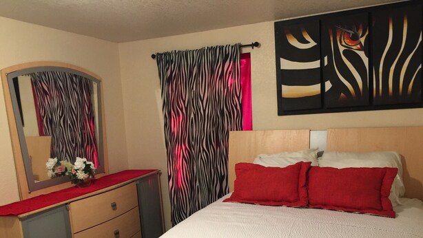 Un dormitorio con cama, cómoda, espejo y cortinas a rayas de cebra.