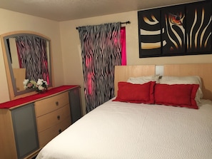 A bedroom with a bed, a dresser, a mirror, and zebra-striped curtains.