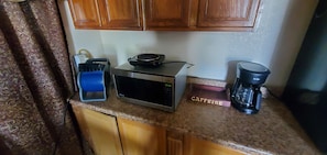 A kitchen counter with a microwave, a coffee maker, and a blue container.