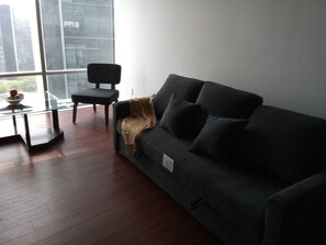 En moderne stue med en mørkegrå sofa, et glasbord og en sort lænestol.