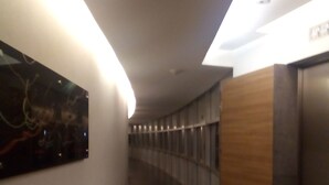 Un couloir avec un comptoir d’accueil en bois, une œuvre d’art accrochée au mur et un luminaire au plafond.