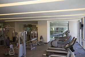 Et fitnesscenter med løbebånd, styrkemaskiner og en glasvæg med udsigt over byen.