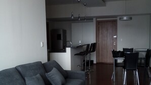 Un salon moderne avec un canapé gris, une table à manger en bois avec des chaises, et un coin cuisine à l’arrière-plan.