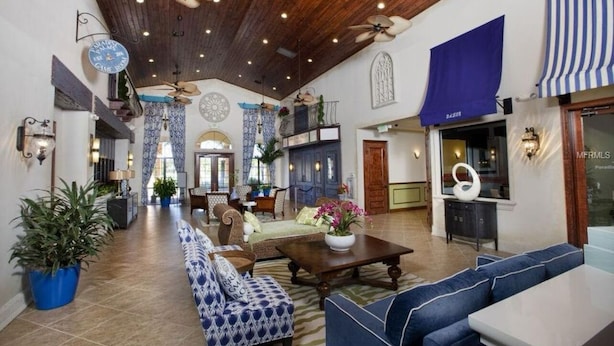 Eine großzügige Lobby mit hoher Decke, Holzbalken und Deckenventilatoren. Es gibt Sitzbereiche mit gestreiften Sofas und einem Couchtisch.