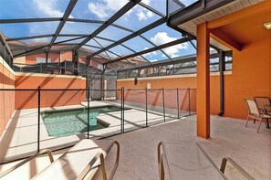 Área de piscina descoberta coberta por uma estrutura de vidro, rodeada por paredes laranja e algumas cadeiras de descanso.