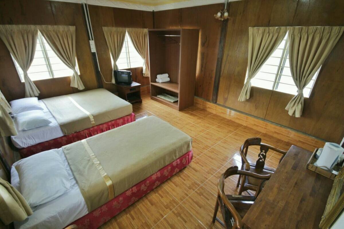 Een kamer met twee bedden, een televisie, een houten garderobe en een bureau met stoelen.