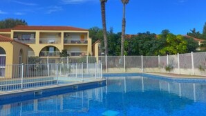 Una piscina con recinzione bianca, un edificio con balconi e palme.