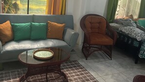 Ein Wohnzimmer mit Sofa, Sessel, Couchtisch und Blick ins Grüne.
