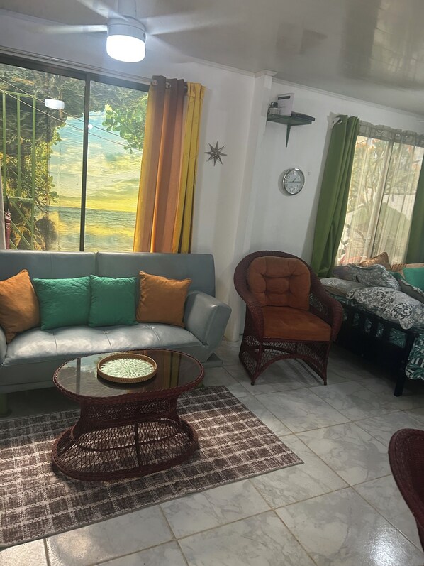 Una sala de estar con sofá, sillón, mesa de centro y vista a zonas verdes.
