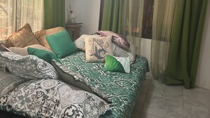 Ein Schlafzimmer mit Bett, grünen Vorhängen, Deckenventilator und Fenster mit Blick auf Bäume.