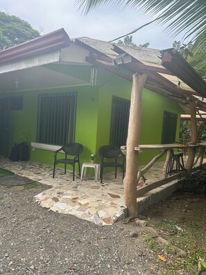 A green building with a tiled patio, two chairs, a small table, and a potted plant. - 🐒CASA MONO VERDE  10 minutes walk to playa blanca, The National Park, Mepe Bus (Cahuita)