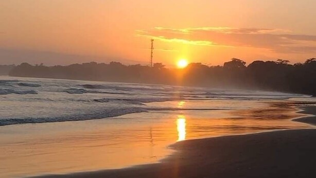 Ein Sonnenuntergang über einem Strand mit ruhiger Wellen und einem wolkenlosen Himmel.