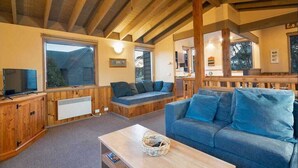 Ein gemütliches Wohnzimmer mit Holzbalkendecke, einem blauen Sofa, einem Fernseher und einem Fenster.