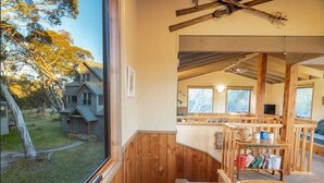 Eine rustikale Holzhütte mit Holzvertäfelungen, einem Schlafzimmer auf dem Dachboden mit schrägem Dach und Blick auf ein Haus und Bäume.