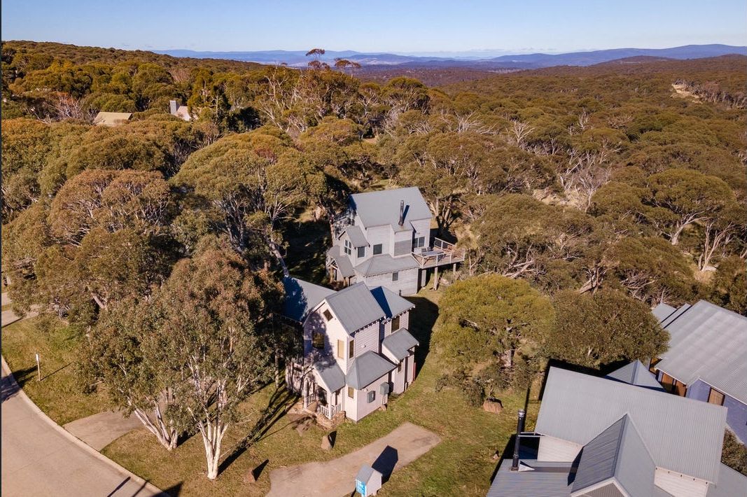 A large, two-story house surrounded by dense trees and a hilly landscape.