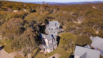 A large, two-story house surrounded by dense trees and a hilly landscape.