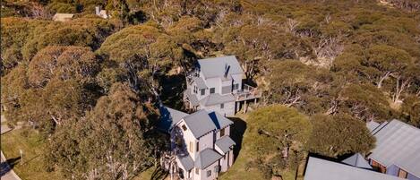 A large, two-story house surrounded by dense trees and a hilly landscape.