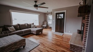 A living room with a sofa, ottoman, and a fireplace. - Country Farmhouse Sleeps 12 with hot tub. (Salmon)