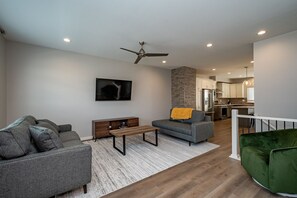 A modern living room with a grey sofa, a coffee table, a TV, and a staircase leading to a kitchen.