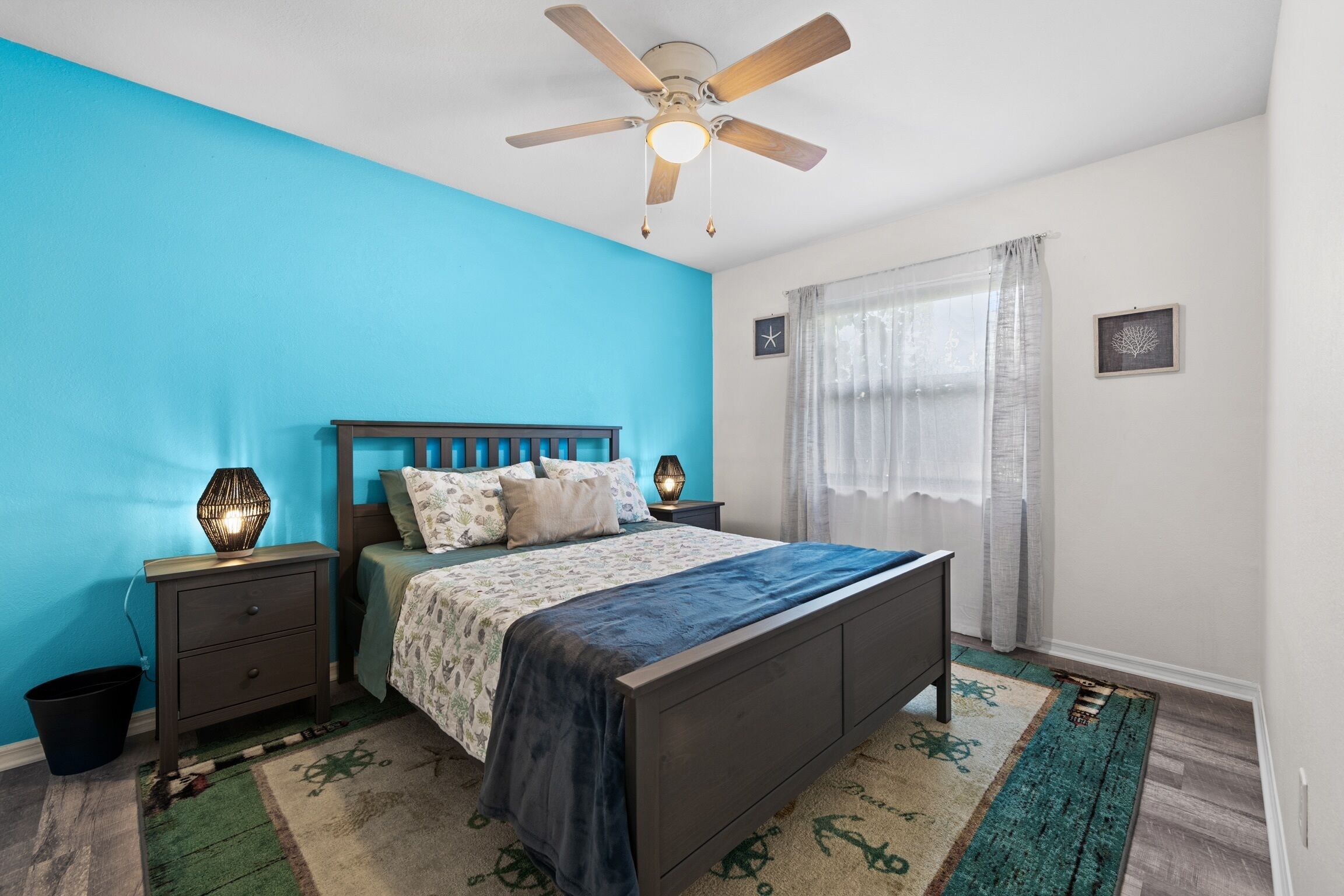 A bedroom with a bed, nightstands, a ceiling fan, a rug, and a window with curtains.