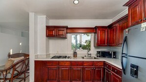 A kitchen with wooden cabinets, a refrigerator, a microwave, and a window.