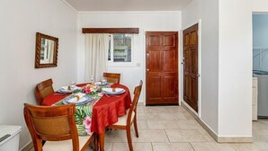 A dining area with a table set for four, wooden chairs, a window with curtains, and a door leading to another room.