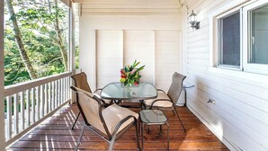 A covered outdoor patio with a table and chairs, surrounded by white walls and a wooden ceiling.