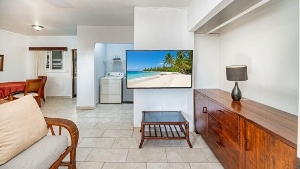 A living room with a TV, wooden furniture, a dining area, and a kitchen.
