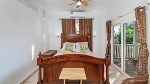 A bedroom with a wooden bed, a small table, a ceiling fan, and a view of the outdoors.