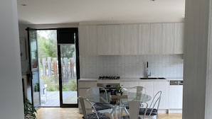 Una cucina moderna con mobili bianchi, un tavolo da pranzo in vetro e sedie, e un pavimento in legno a spina di pesce.