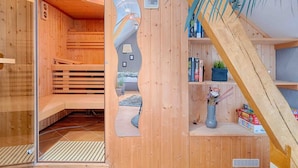 Una sauna de madera con puerta de vidrio, un banco y una estantería con libros y un florero.