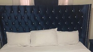 Una cama con cabecera capitonada, ropa de cama blanca y una toalla dispuesta en forma de corazón sobre la cama.