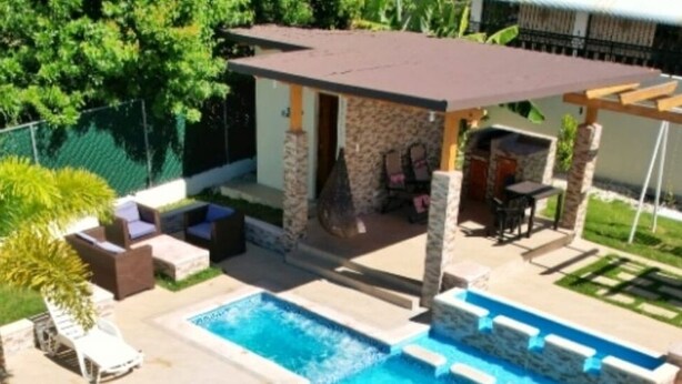Un área de piscina con una pérgola, mobiliario exterior y una estructura de piedra.