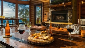 Interior de una cabaña de madera con una mesa de comedor dispuesta para una comida, mostrando queso, vino y pan.