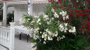 A white building with a balcony, a table with chairs, and potted plants with white and red flowers. - The Apartment is on the Ground Floor - 1 Entire Floor 110 m2 (Rab)