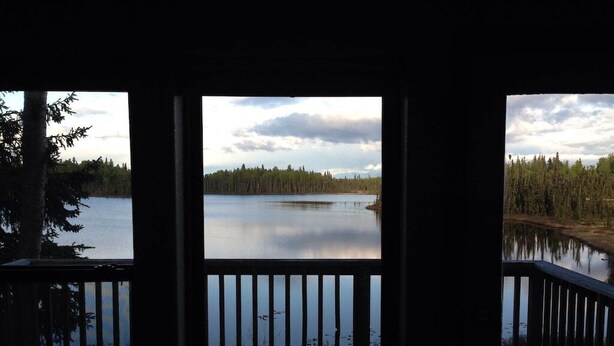 Vista desde una terraza de madera con vista a un lago tranquilo rodeado de árboles.