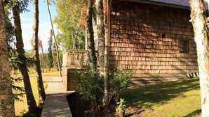 Una cabaña de madera con un porche y un área cercada, rodeada de árboles.