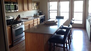 Una cocina con armarios de madera, estufa, microondas e isla grande con taburetes de bar.