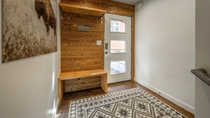 Un banco de madera, un letrero de bienvenida y una alfombra estampada en un pasillo con una puerta.