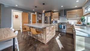 Una cocina moderna con una isla central, armarios de madera, electrodomésticos de acero inoxidable e iluminación colgante.