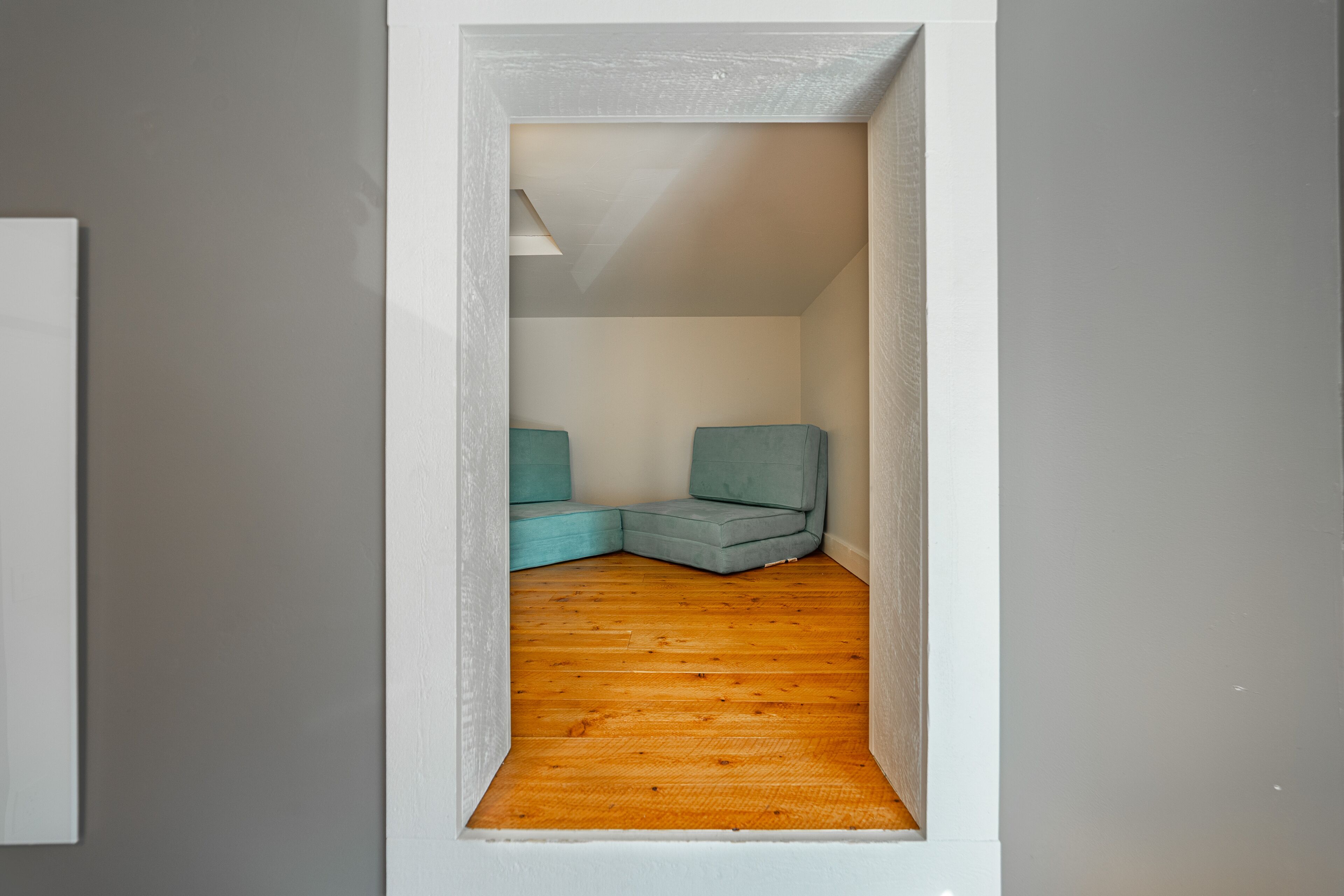 A narrow hallway with wooden flooring and two teal chairs in a corner.