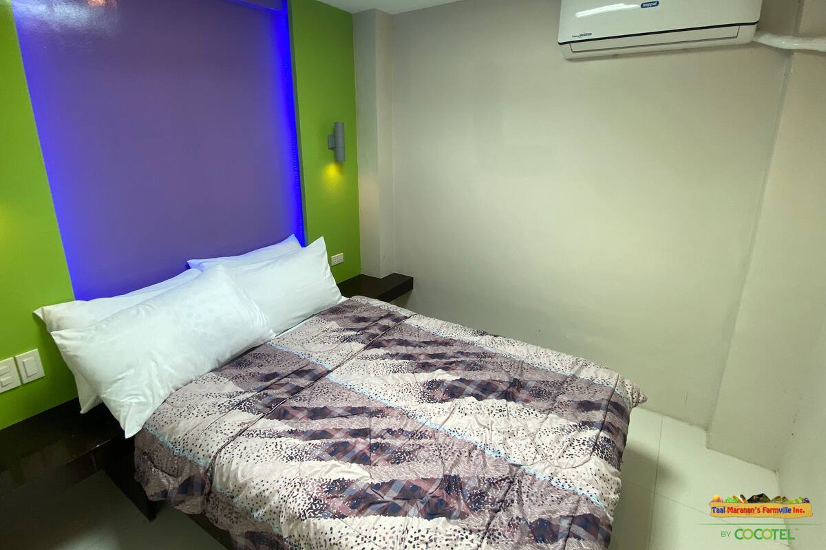 A bedroom with a bed, green and purple walls, a white air conditioner, and a nightstand.