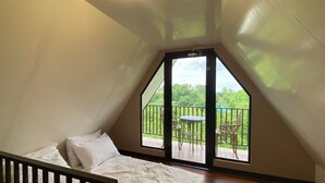 A bedroom with a sloped ceiling, a bed with white bedding, and a balcony with a table and chairs. - Taal Maranan Farmville Inc. (Taal)