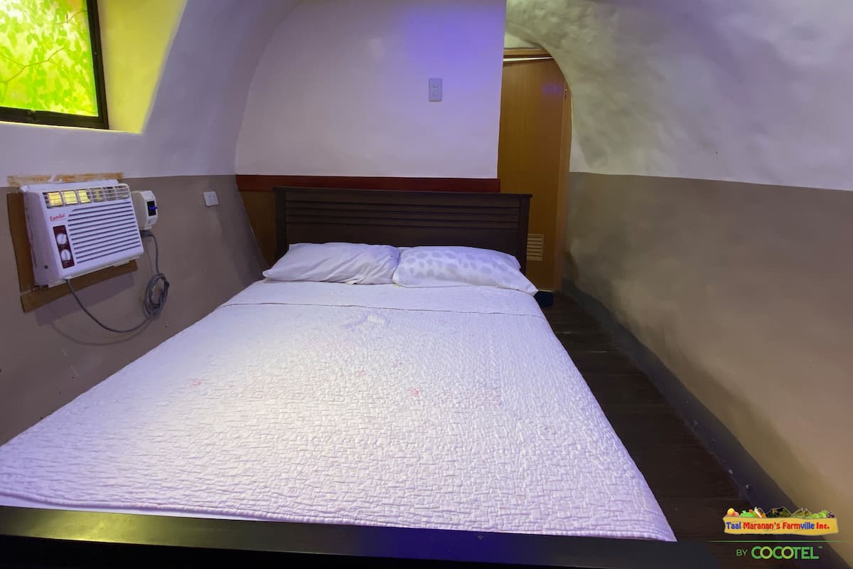 A single bed with a textured white mattress, a wooden headboard, and a wall-mounted air conditioning unit.