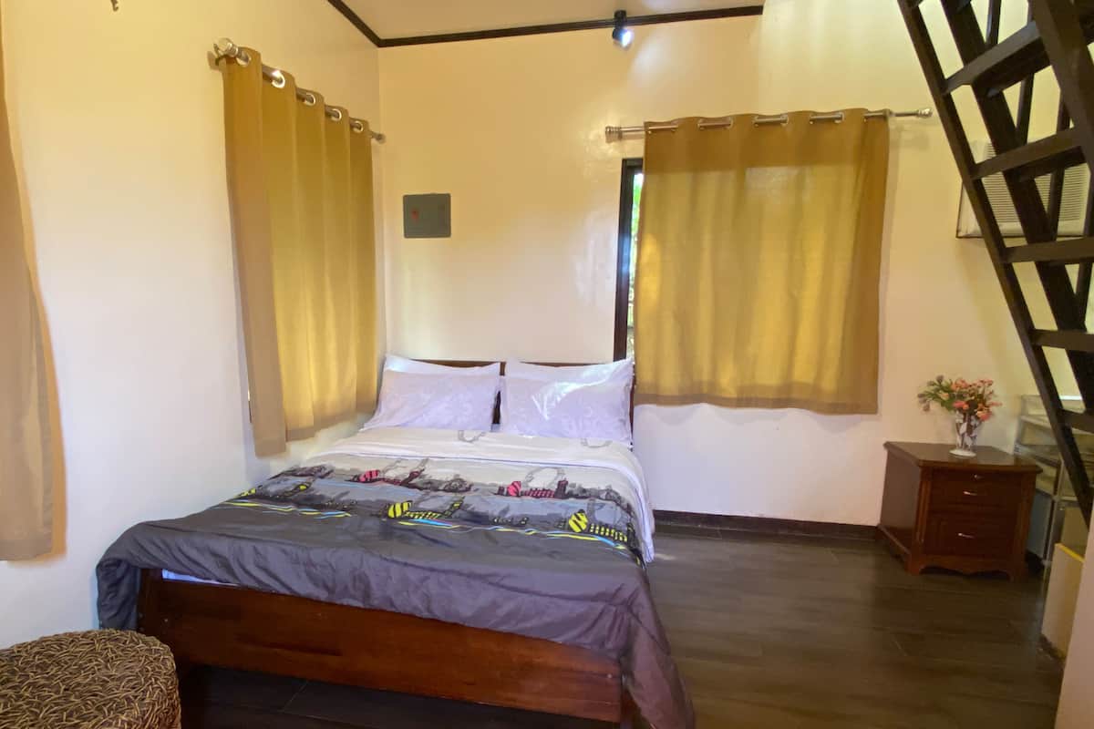A bedroom with a bed, curtains, a nightstand, and a wooden ladder.