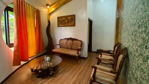 A room with a round wooden table, a sofa, and two armchairs. There is a painting on the wall and a window with curtains. - Taal Maranan Farmville Inc. (Taal)